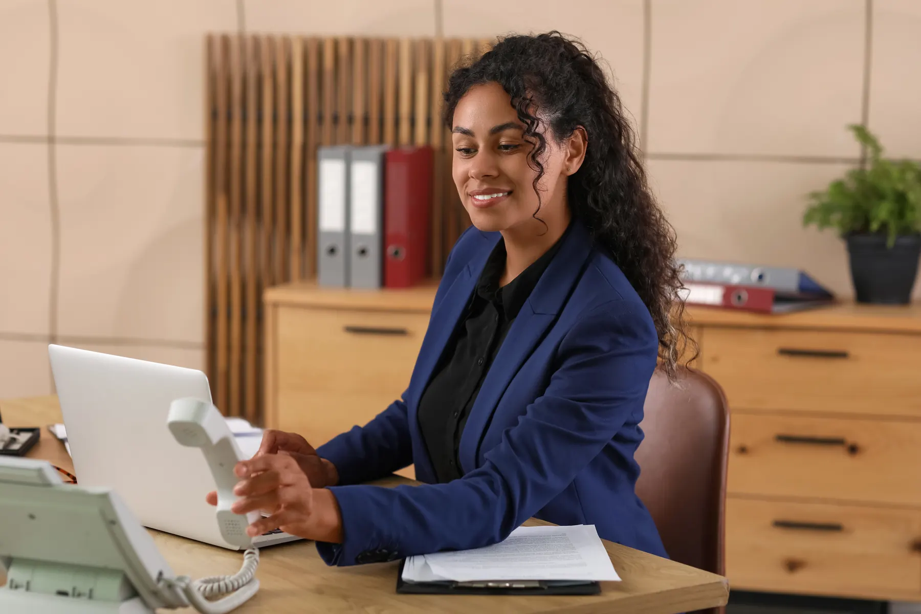 An attorney at her desk picking up the office phone beside a laptop and case files